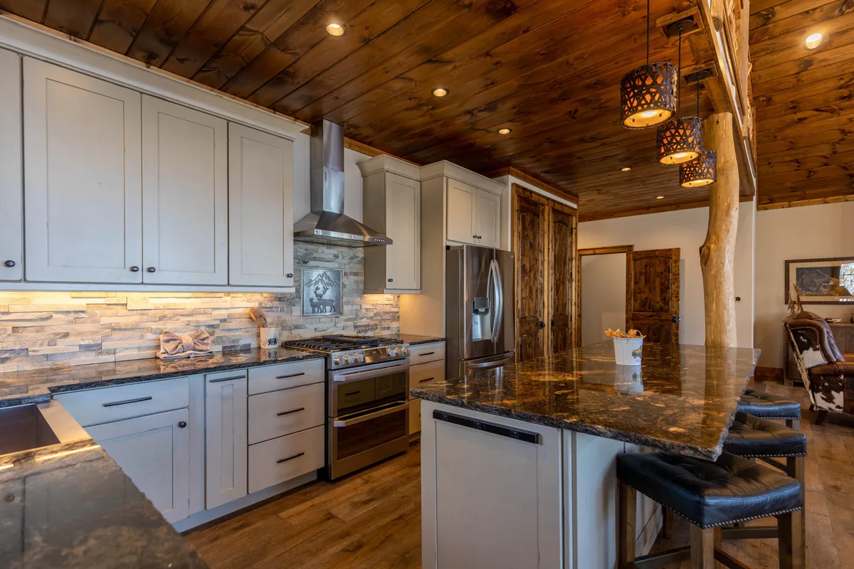 A modern kitchen with a granite countertop, stainless steel appliances, wooden beams, and decorative pendant lights. The space is open and inviting, ideal for preparing meals after active days outside or entertaining family and friends.