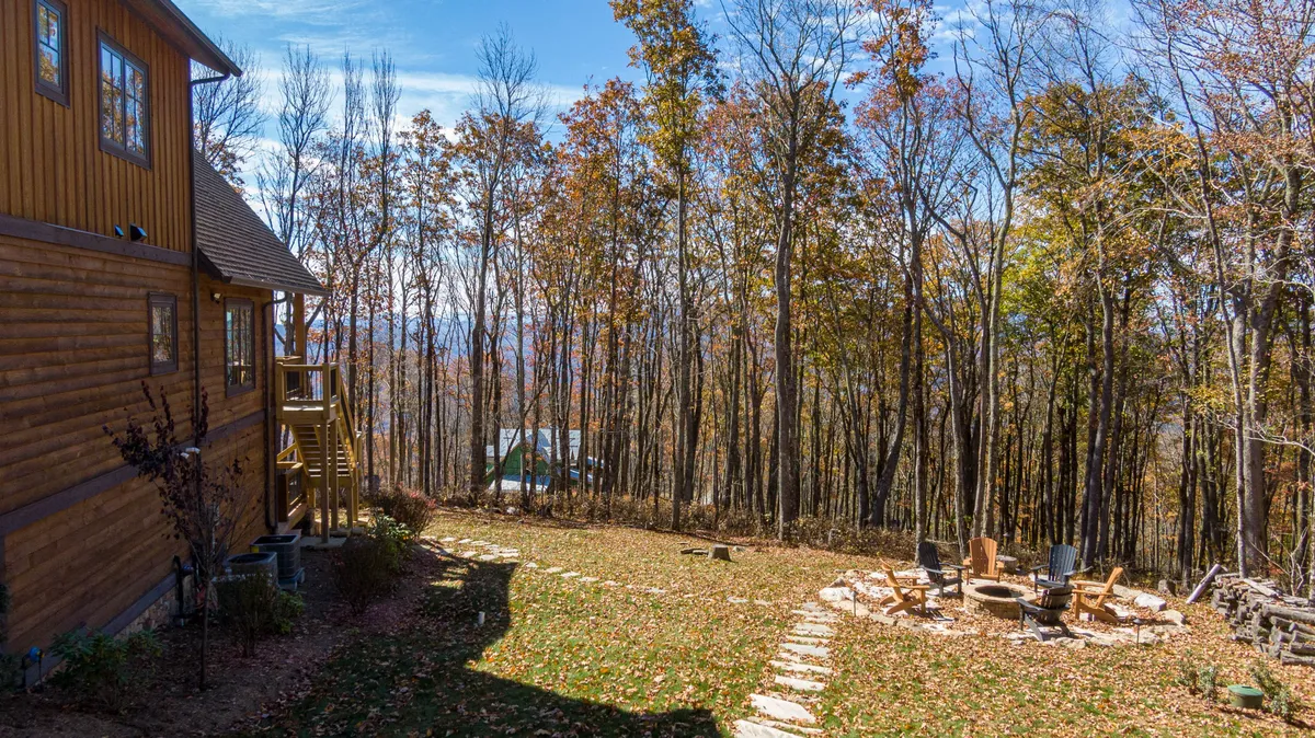 An inviting wooden deck with a fire pit and comfortable seating, surrounded by trees and natural landscaping. The scene suggests evening gatherings, storytelling, and enjoying the mountain air with friends or family.