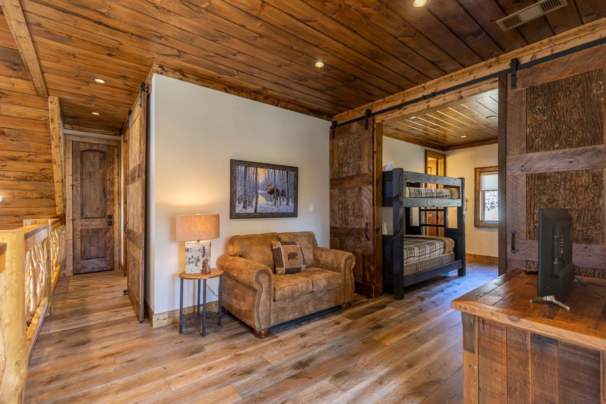 A cozy bunk room setup with bunk beds, a comfortable sofa, a reading lamp, and wall art. The warm lighting and furnishings create a relaxed space suitable for families, kids, or groups of friends to gather, play games, or enjoy quiet moments together.