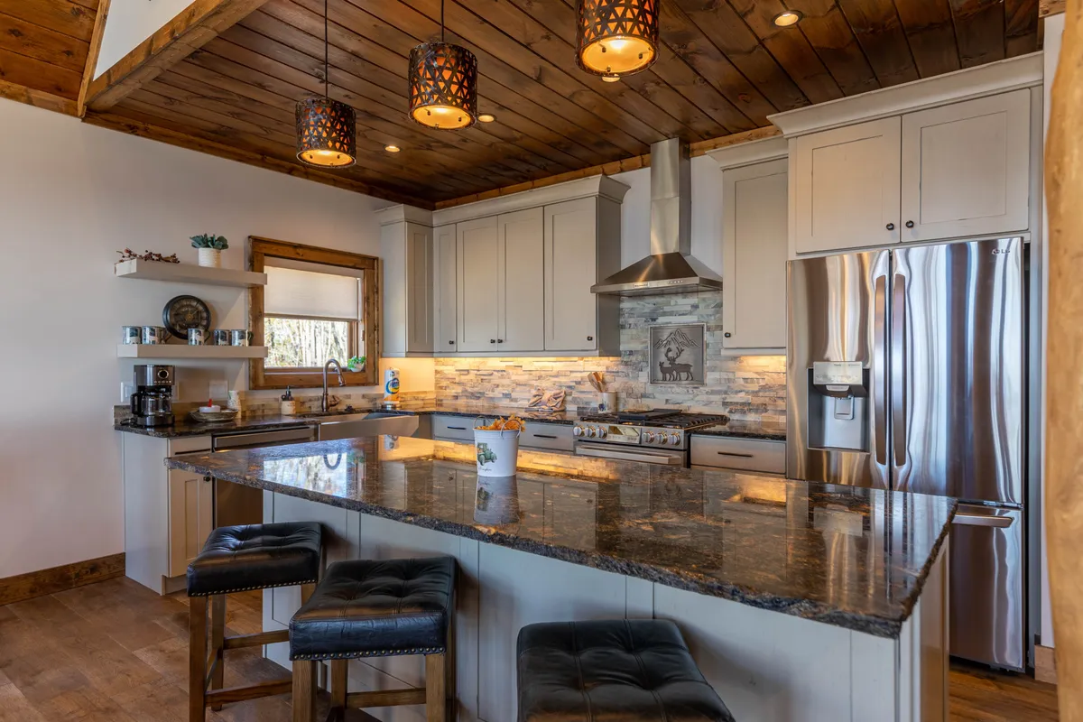 A close-up perspective of the kitchen area, emphasizing the granite countertop, pendant lights, rich cabinetry, and sleek stainless steel appliances. The inviting setup suggests a space for entertaining and casual family gatherings.