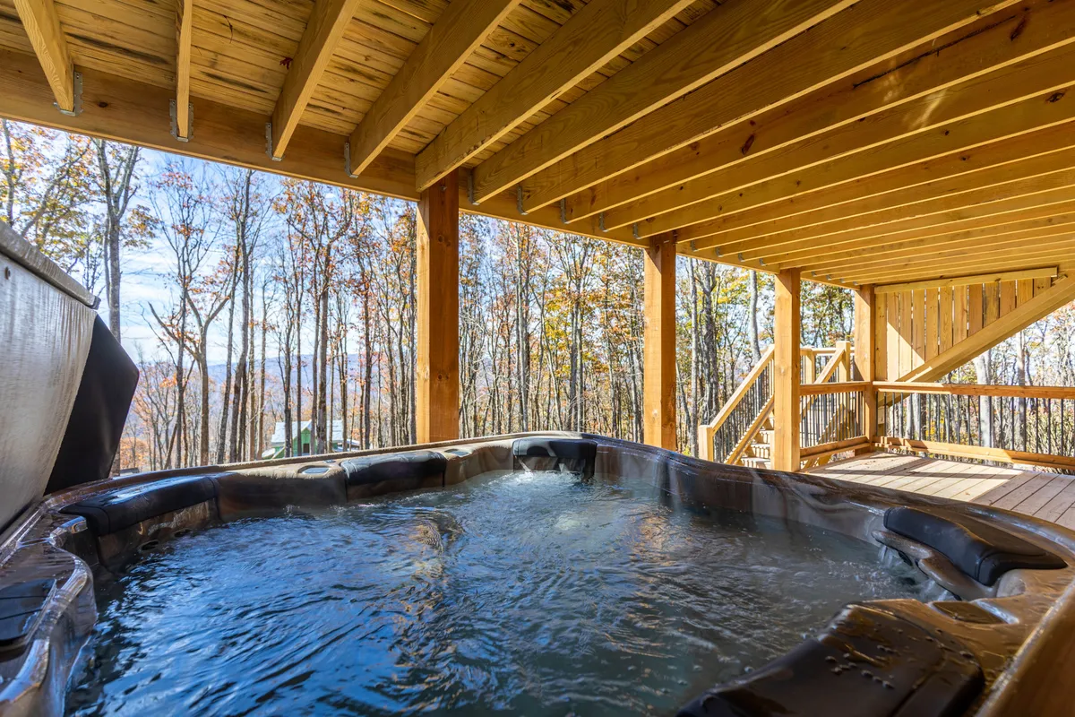 A serene hot tub sits on a wooden deck surrounded by lush forest, offering a private retreat with immersive nature views. The warm, bubbling water promises relaxation and a luxurious outdoor experience.