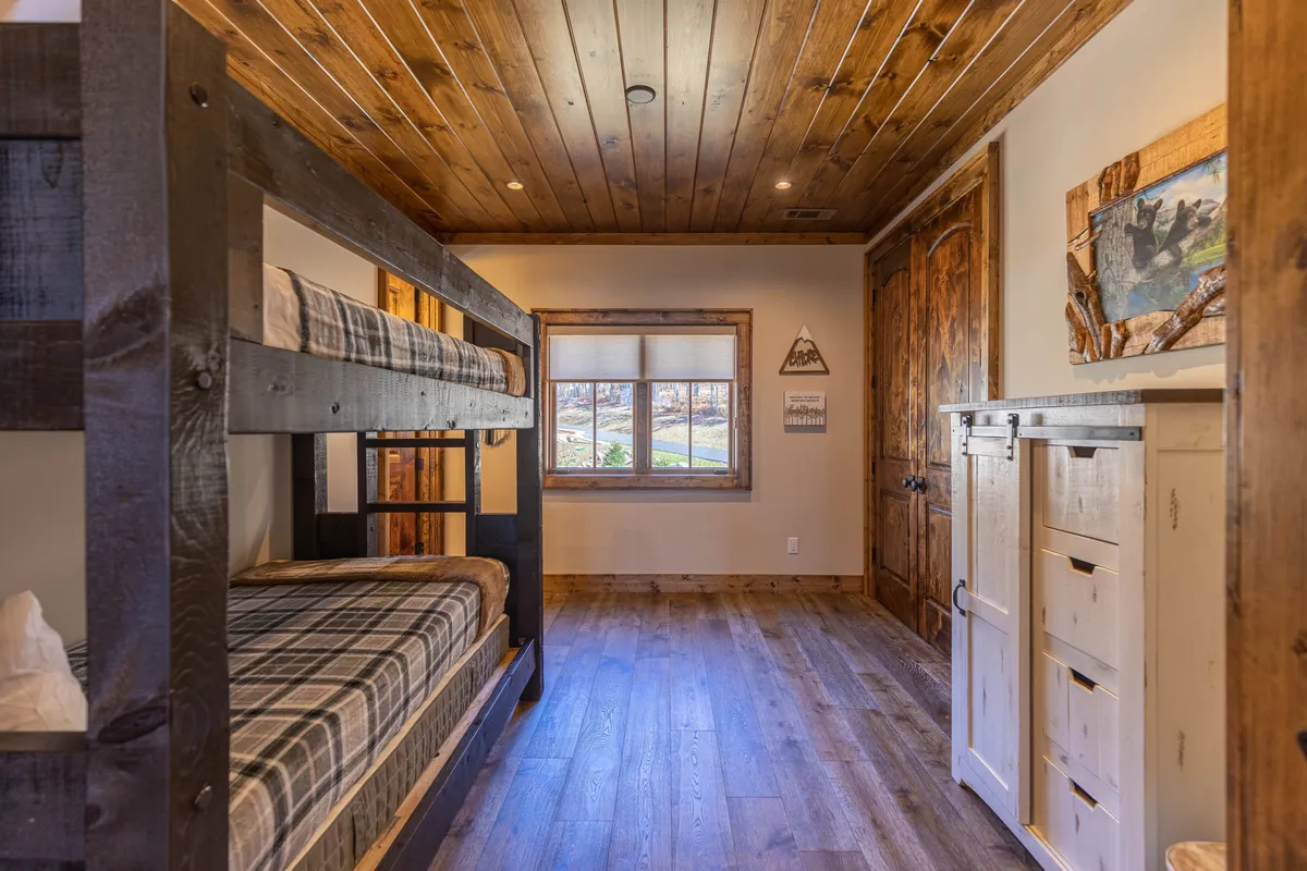 A warm, inviting bunk room featuring wooden bunk beds, a ceiling of exposed beams, and soft natural light spilling through a window. The scene evokes a sense of fun and togetherness, with hints of imaginative play and memorable family sleepovers.