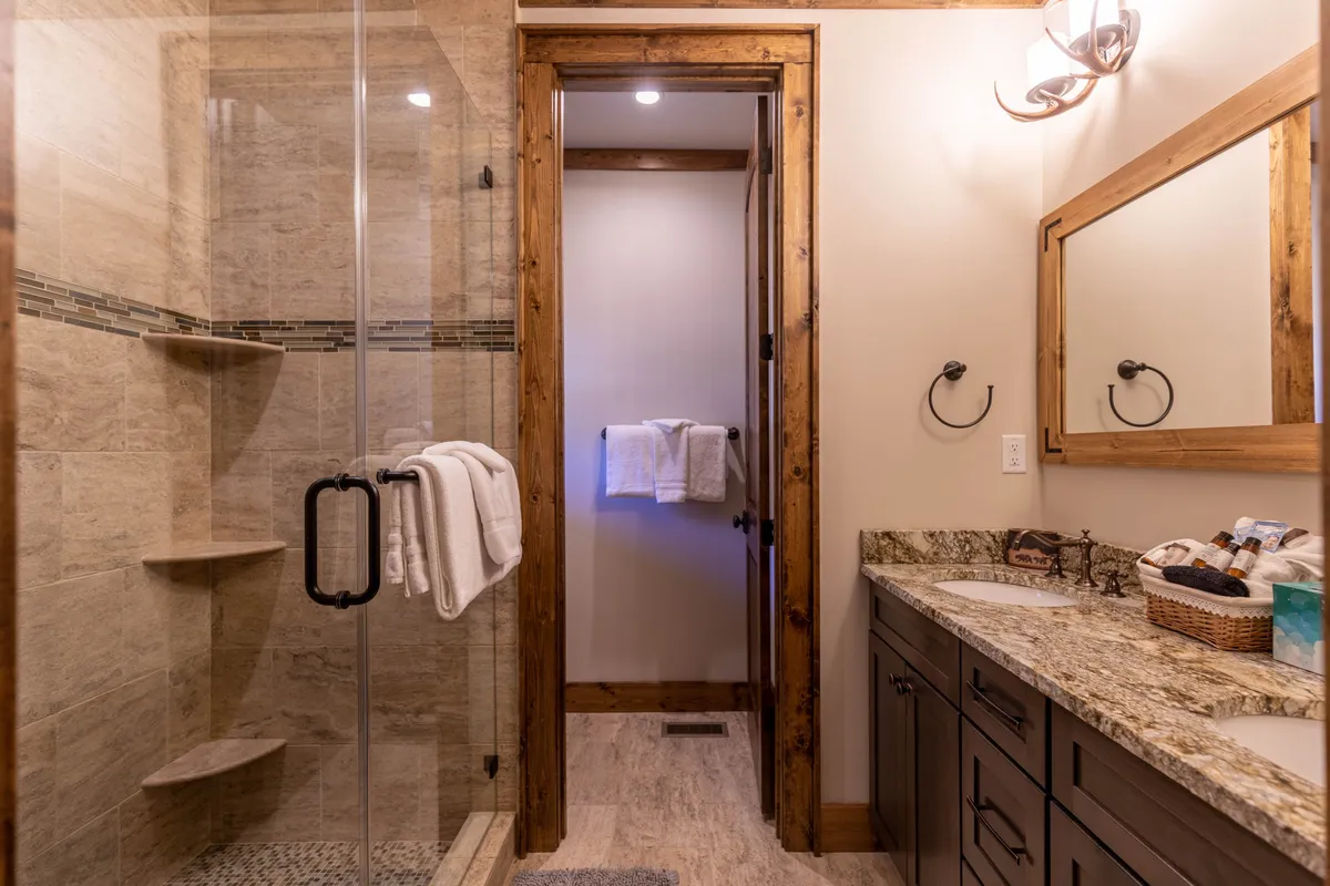 A spa-inspired bathroom with a glass shower, double vanity, wooden accents, and a granite countertop. The space is filled with serene natural light, creating a luxurious and calming environment for self-care and relaxation.