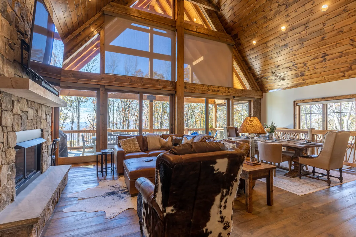 A welcoming living and dining space with an impressive stone fireplace, expansive windows revealing mountain views, comfortable seating, and a dining table set for family meals. The ambiance is warm, inviting, and ideal for both relaxation and celebration.